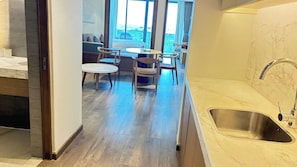 A modern kitchen with a sink, wooden flooring, and a dining area with chairs and a table. - DIAMOND SUITE KEM BEACH (Phu Quoc)
