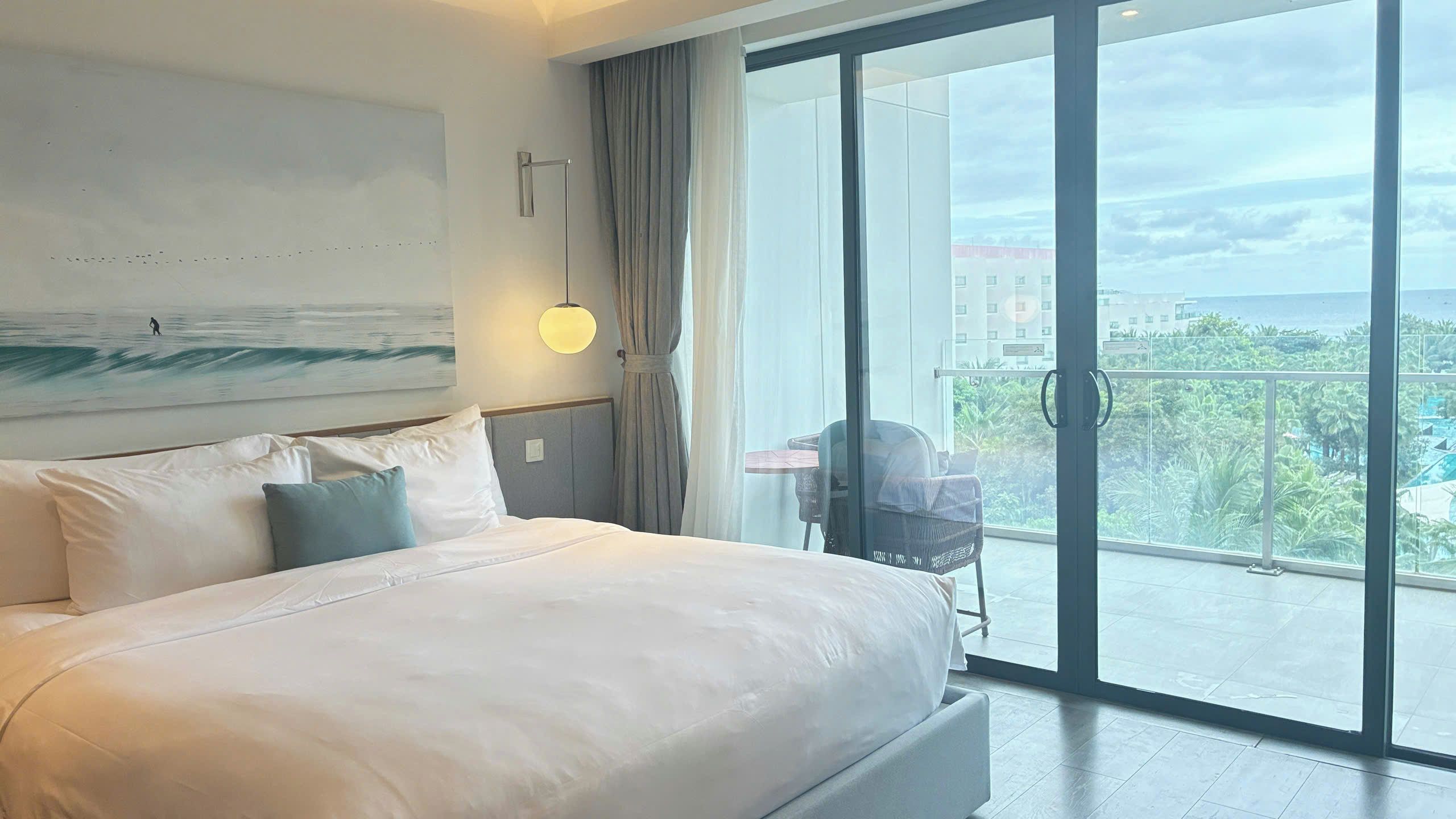 Habitación de hotel con una cama grande, vistas a la ciudad y un balcón con una silla.