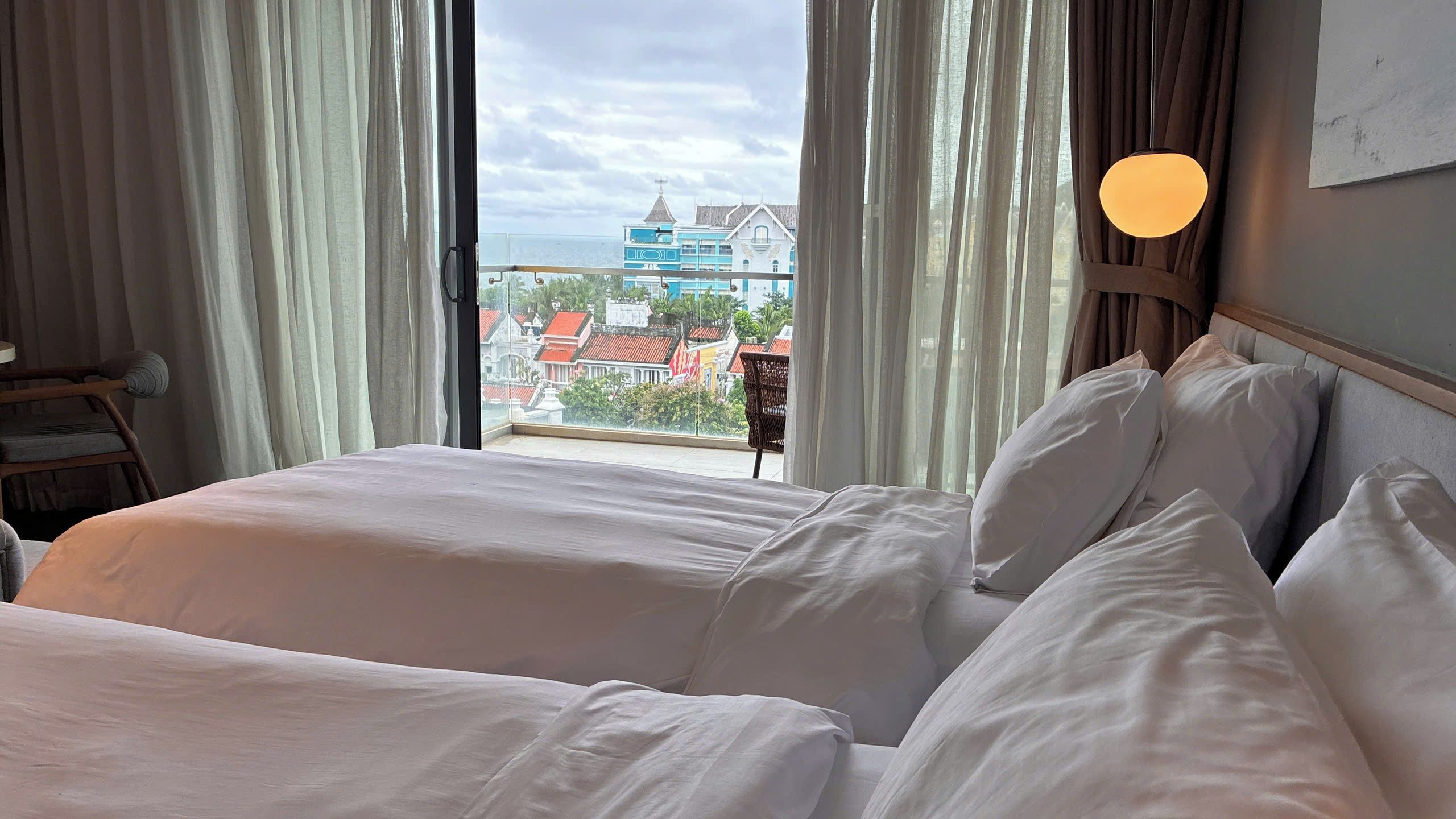 Quarto de hotel com duas camas, vista para edifícios e varanda.