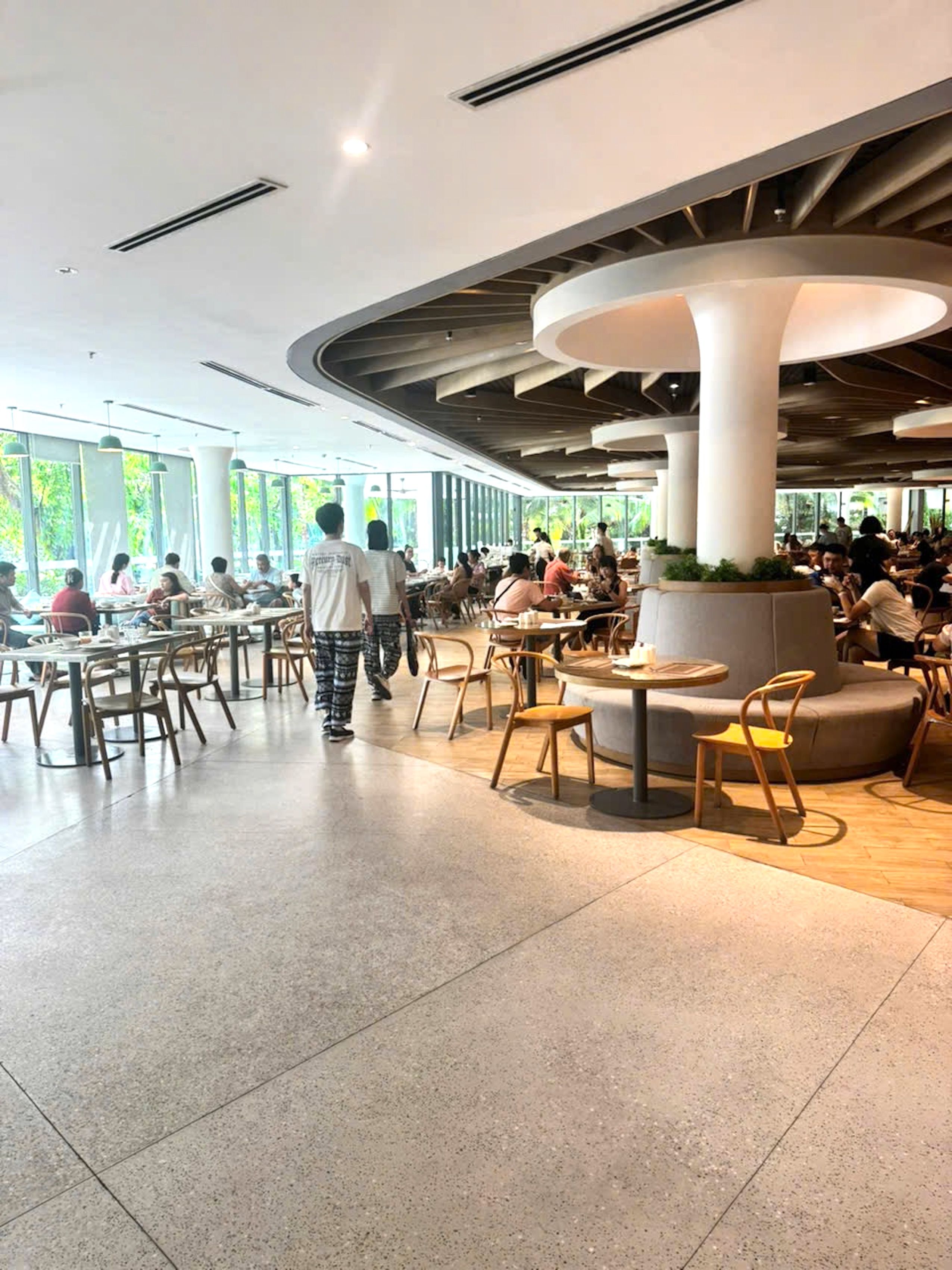 Un amplio comedor interior con diversas opciones de asientos, incluidas mesas y sillas, y una estructura de columna central.