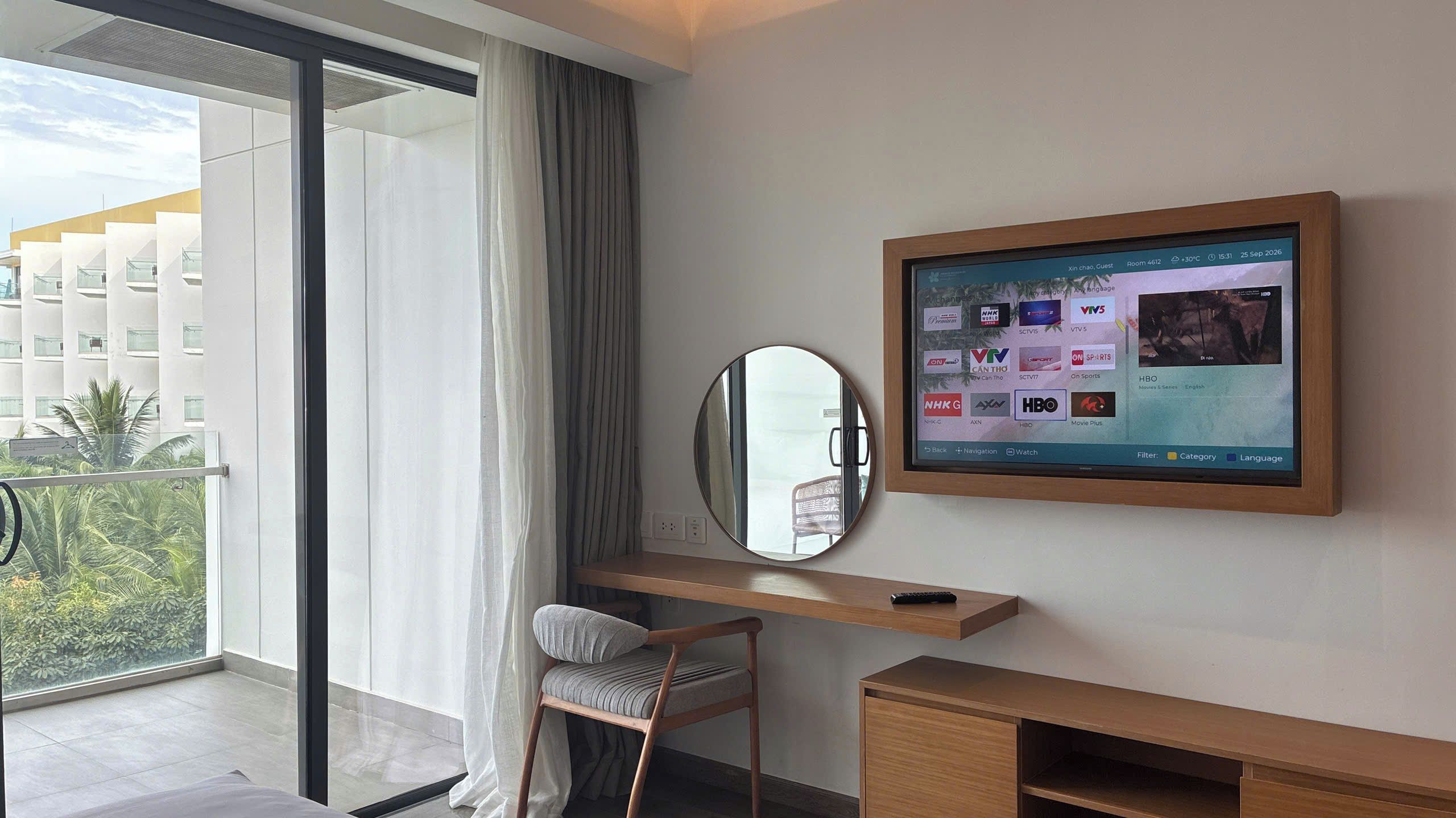 Ein Hotelzimmer mit einem großen an der Wand befestigten Fernseher, einem Schreibtisch mit Stuhl und Blick auf ein Gebäude.