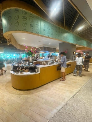 A food counter with various dishes and utensils, a person serving food, and a counter with a patterned design.