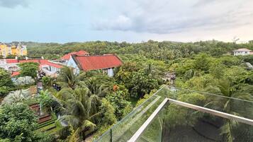 A high-rise building with a glass balcony overlooking a lush green landscape and several buildings with red roofs.