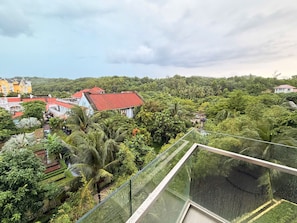 A high-rise building with a glass balcony overlooking a lush green landscape and several buildings with red roofs.