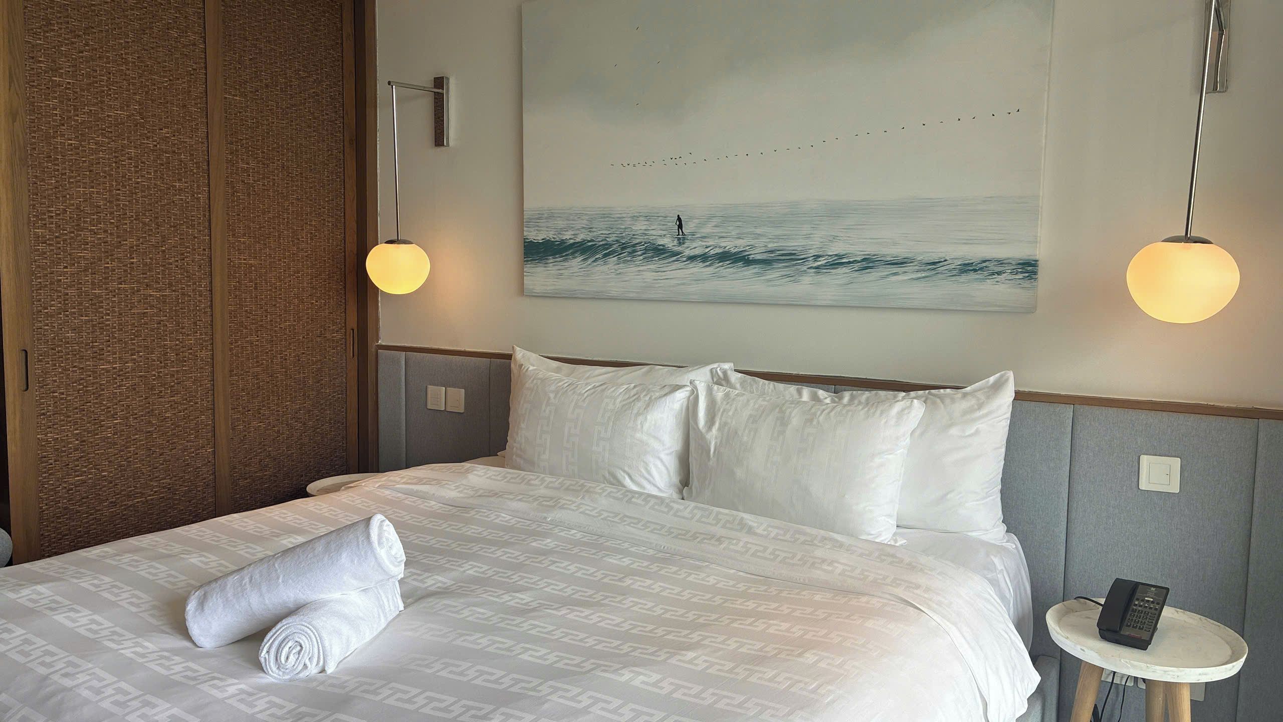 A hotel room with a bed, a painting of birds, and a phone on a bedside table.