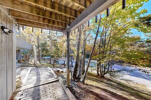 A covered outdoor area with a wooden deck, a view of a road, and trees with autumn foliage. - Winhall townhome with ski mudroom and Bromley slope views from the balcony (Winhall)
