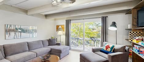 A modern living room with a sectional sofa, a small round coffee table, a side table, a floor lamp, and a television on a wooden shelf.
