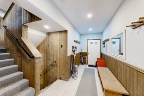 A hallway with a wooden staircase, a bench, a door, and a window. - Winhall townhome with ski mudroom and Bromley slope views from the balcony (Winhall)