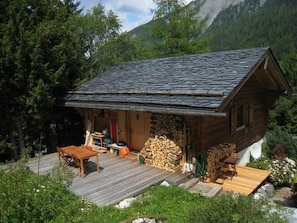 A wooden cabin with a sloped roof, a wooden deck, and a stack of firewood. - Chalet in Praz-de-Fort im Val Ferret by Interhome (Champex)