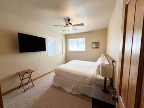 A bedroom with a bed, a ceiling fan, a mounted TV, and a window. - River Sol - Riverfront, Hot Tub, S out Resort, Gorgeous Family Retreat (Bend)