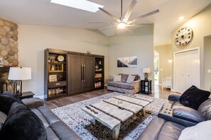 Una sala de estar con ventilador de techo, chimenea, estantería, sofá y mesa de centro.