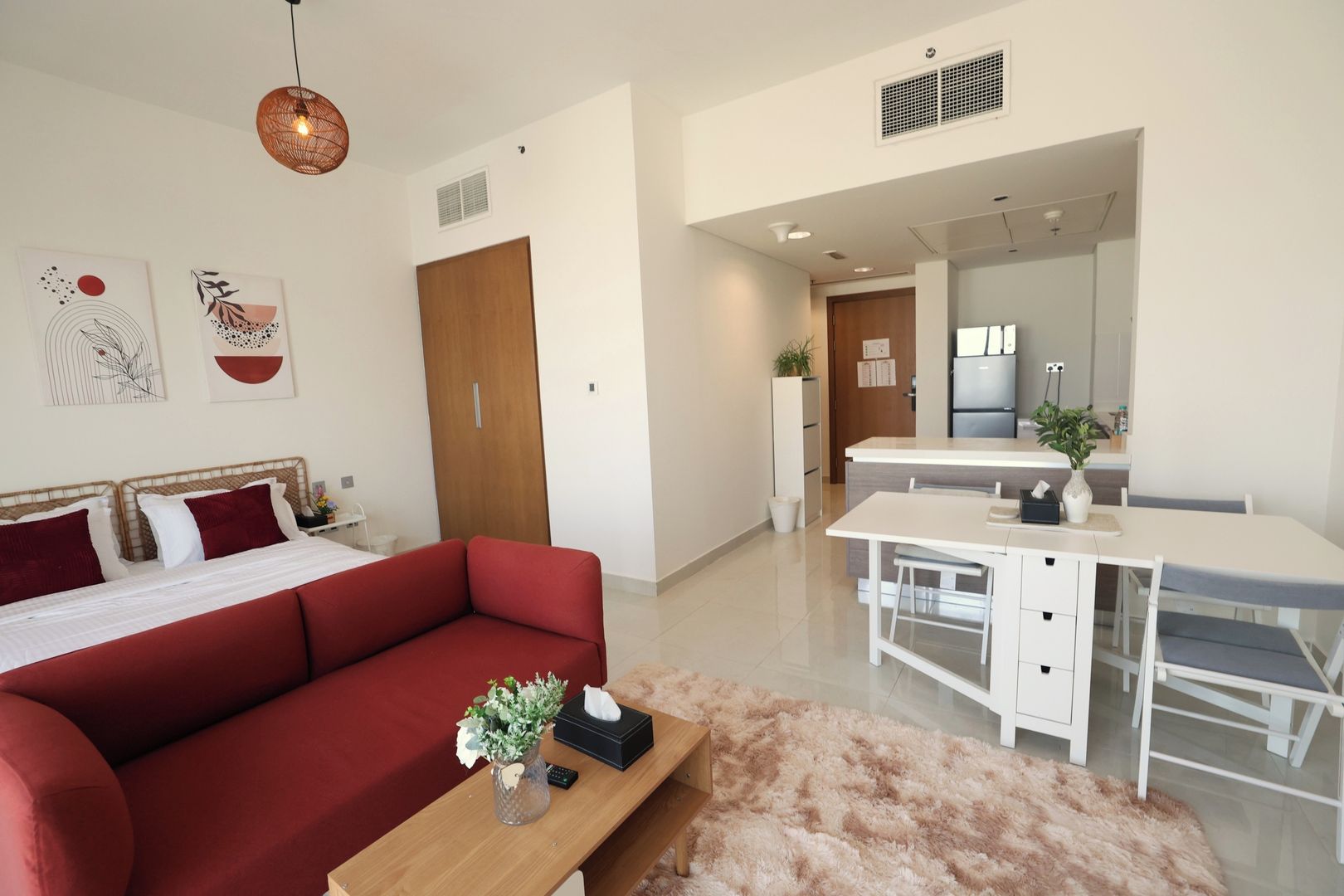 A modern bedroom with a red sofa, a wooden bedside table with a vase, and a white bed.