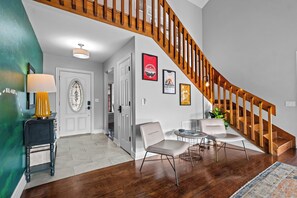 A staircase with wooden railings, a dining area with chairs and a table, and a hallway with a door and a lamp. - The Amelia @ Coler Creek: Private Hot Tub > Fire Pit > Bikers Lounge (Bentonville)