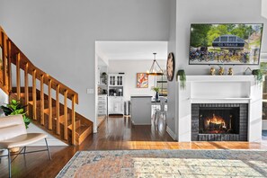 Ein modernes Wohnzimmer mit Kamin, einer Treppe und einer Küche im Hintergrund.