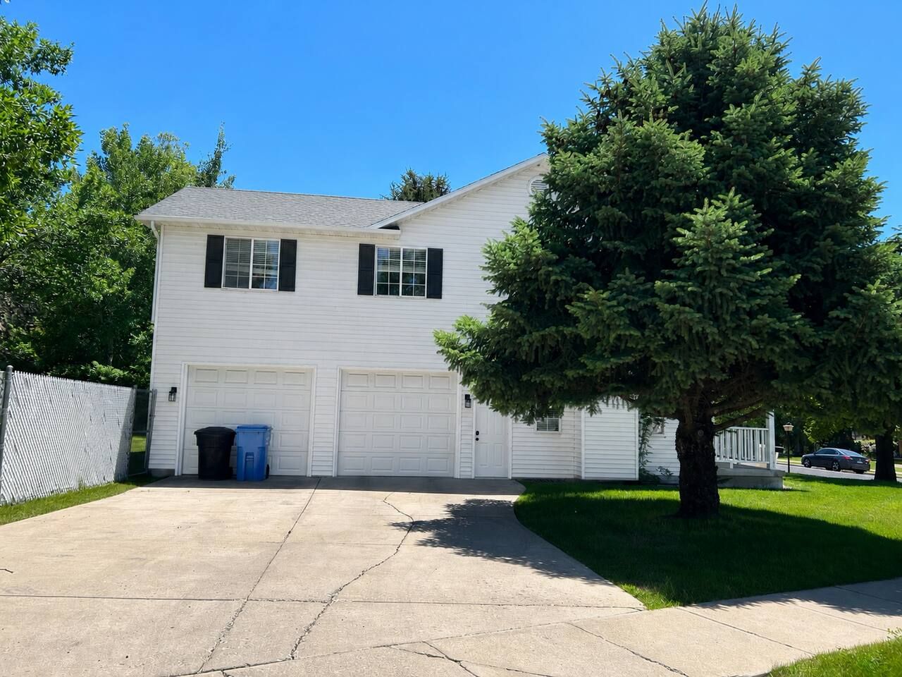A single-story white house with a garage, a tree in front, and a clear blue sky.