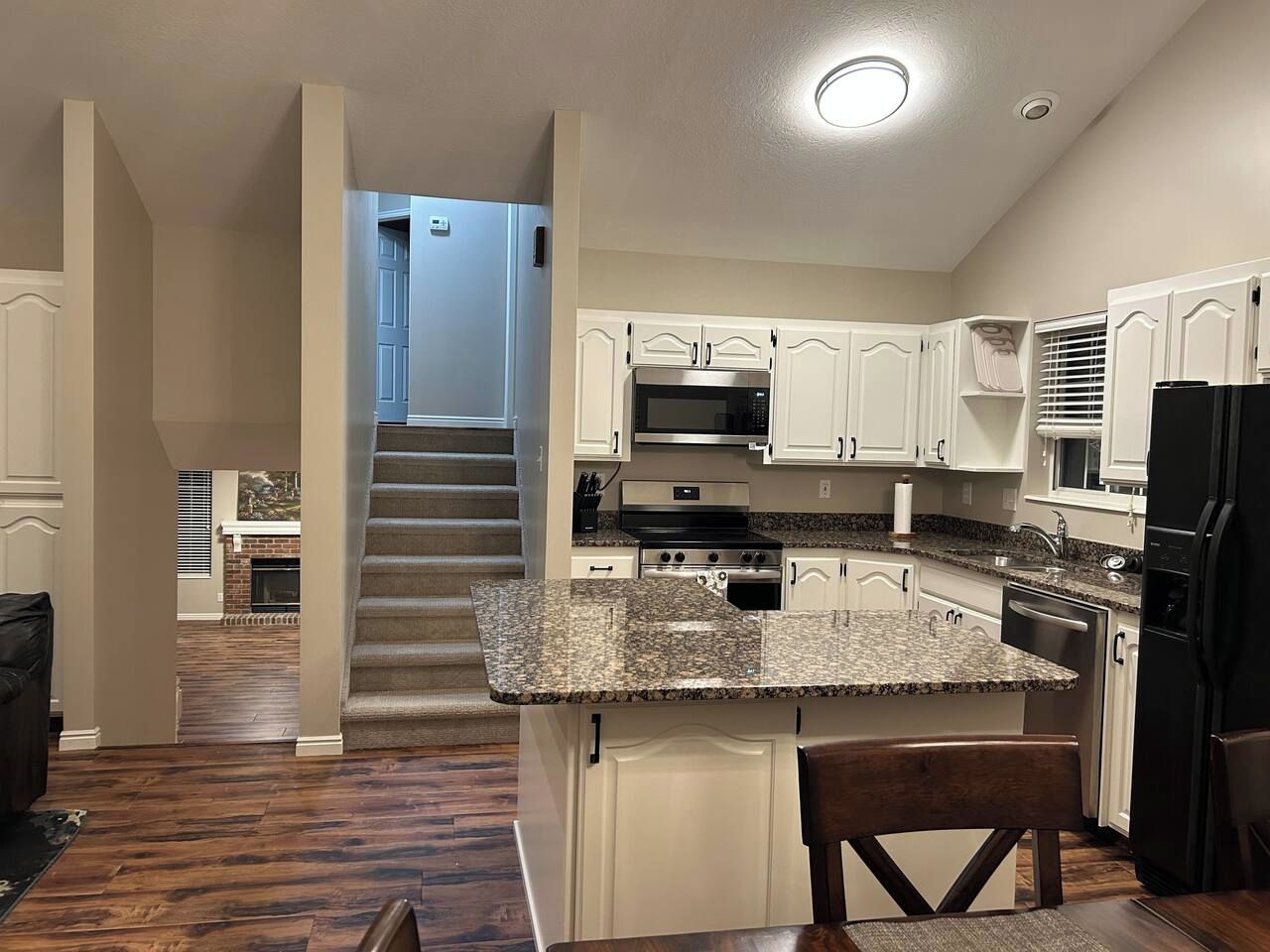 A kitchen with a central island, white cabinets, stainless steel appliances, and a staircase leading to another level.