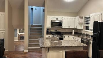 A kitchen with a central island, white cabinets, stainless steel appliances, and a staircase leading to another level.