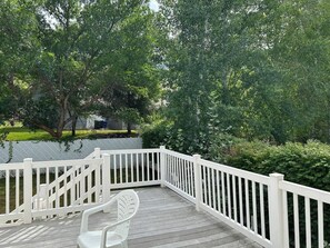 A wooden deck with white railings, surrounded by lush greenery and trees.