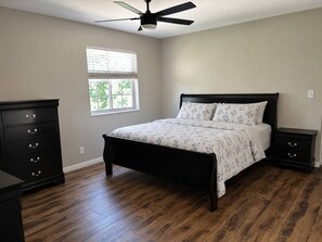 A bedroom with a bed, a dresser, a nightstand, a ceiling fan, and a window with blinds.