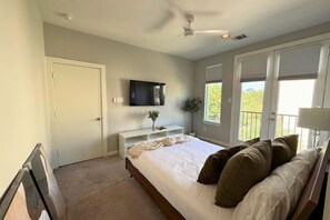 Ein Schlafzimmer mit Bett, Fernseher, Fenster und Deckenventilator.