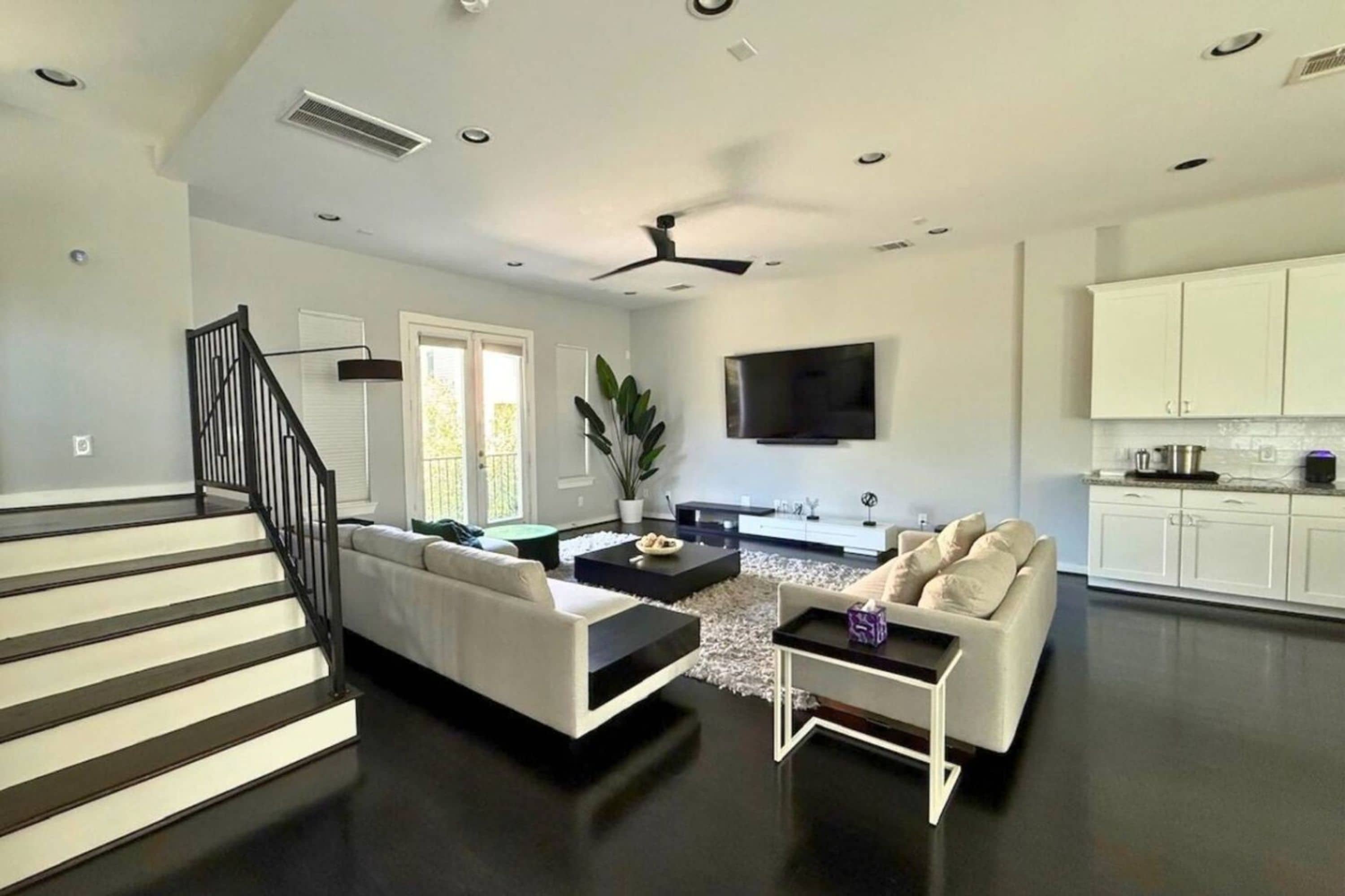 A modern living room with a staircase, a flat-screen TV, and a kitchen area.