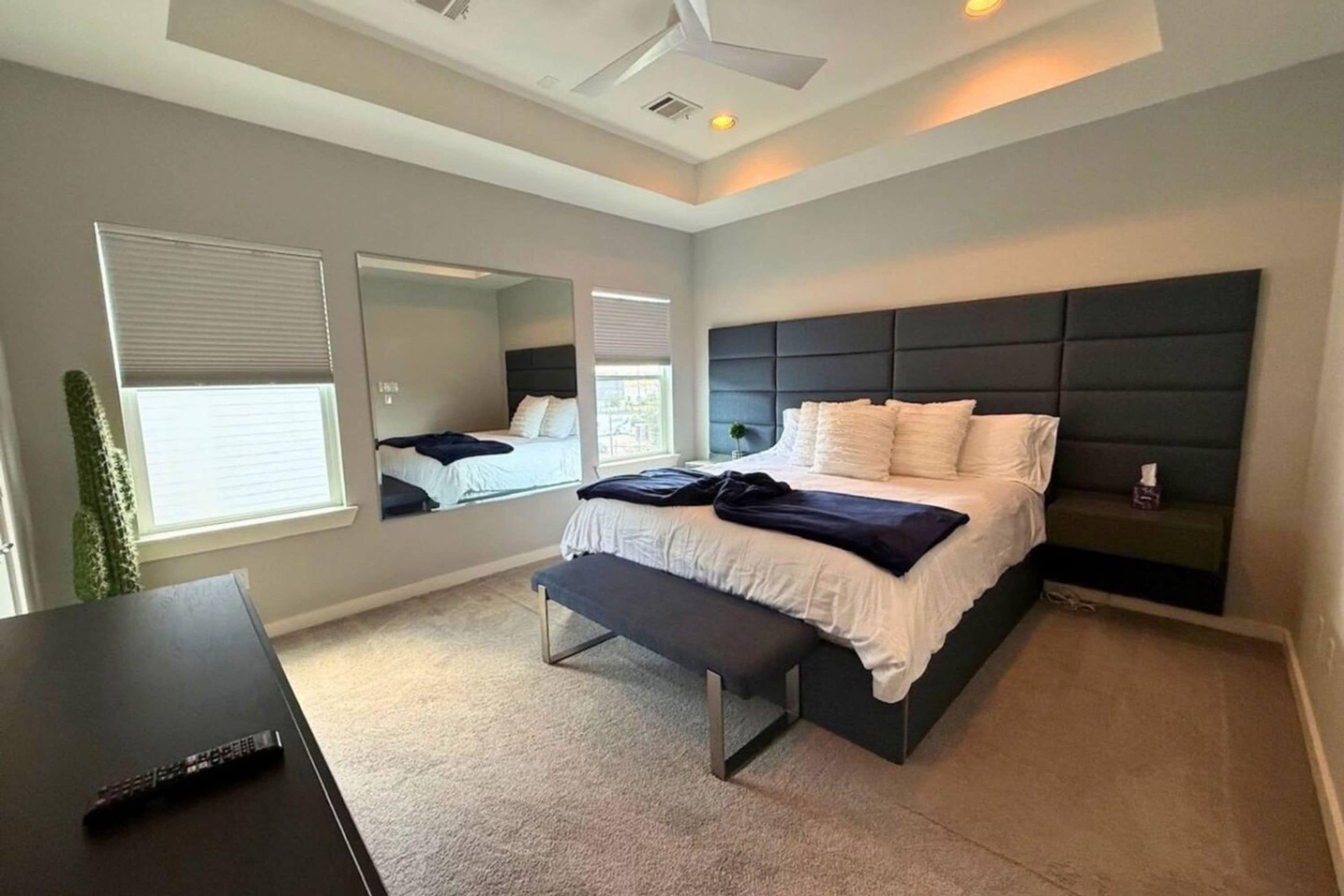 A modern bedroom with a large bed, a bench, a desk, and a mirror.