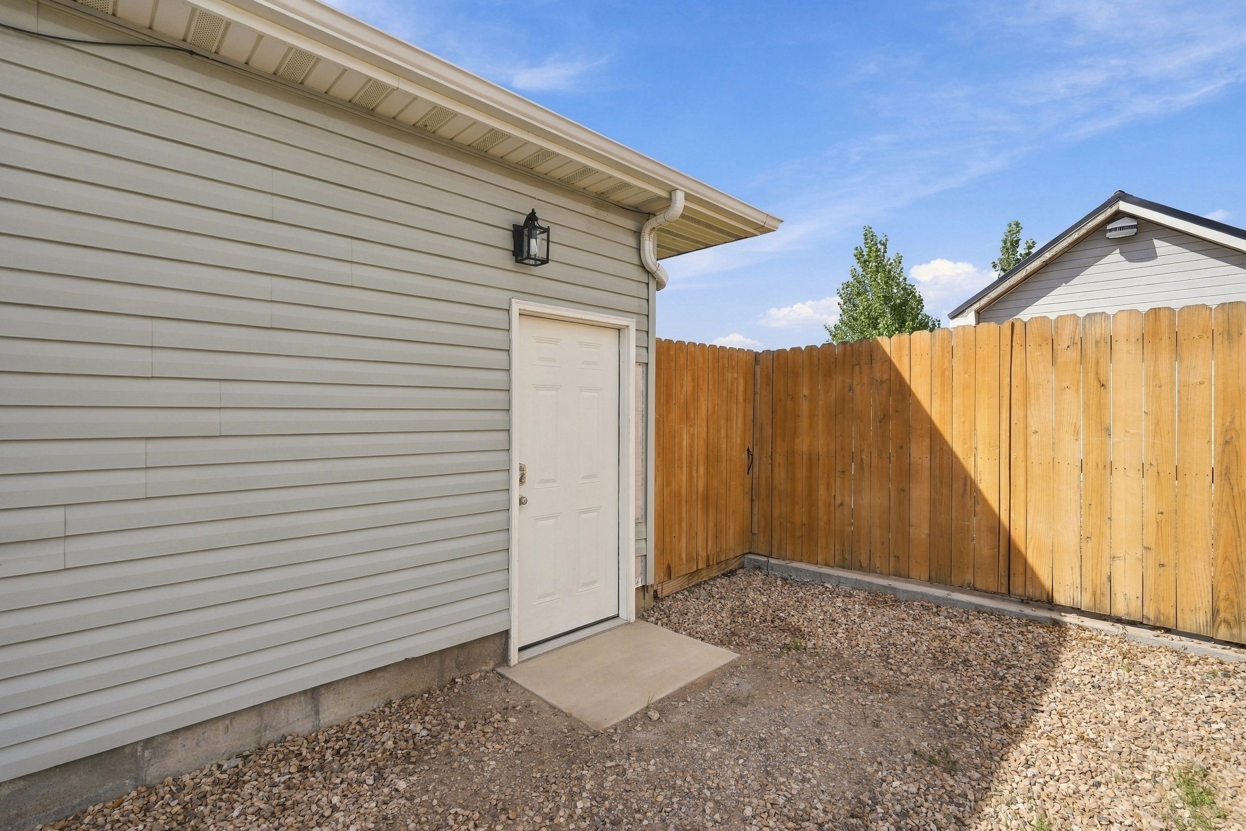 A residential property with a garage door, a wooden fence, and a gravel driveway.