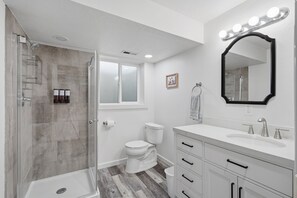 Un baño con ducha, inodoro, tocador y espejo con iluminación.