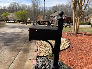A mailbox with a number plate, a street lamp, and a residential area with houses and trees.