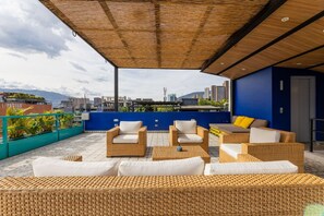A rooftop terrace with wicker furniture, a view of the cityscape, and a blue wall. - Utopia 4 East - Cosmopolitan Loft Self Check-in AC (Medellín)