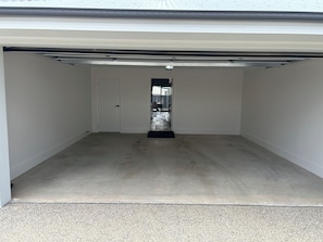 A garage with a concrete floor, white walls, and a closed door. - Silverwoods Retreat I Lake Mulwala & Golf - Your perfect Yarrawonga getaway! (Yarrawonga)