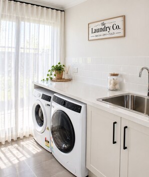 Pesuhuoneessa on kaksi etuaukosta täytettävää pesukonetta, pesuallas ja sen yläpuolella on kyltti, jossa lukee: »The Laundry Co.».