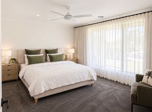 A bedroom with a bed, two nightstands, a ceiling fan, a window with sheer curtains, and a chair. - Silverwoods Retreat I Lake Mulwala & Golf - Your perfect Yarrawonga getaway! (Yarrawonga)