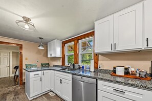 Eine Küche mit weißen Schränken, einer Granit-Arbeitsplatte, einem Geschirrspüler und einem Fenster mit Blick auf Grünflächen.