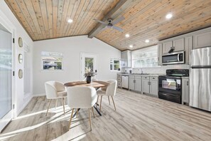 A modern kitchen with white cabinets, stainless steel appliances, and a wooden ceiling.