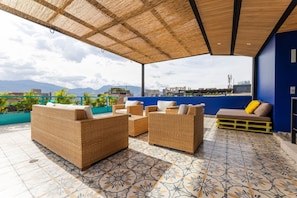 Eine Dachterrasse mit Korbmöbeln, einem gemusterten Boden und Blick auf die Stadtlandschaft.