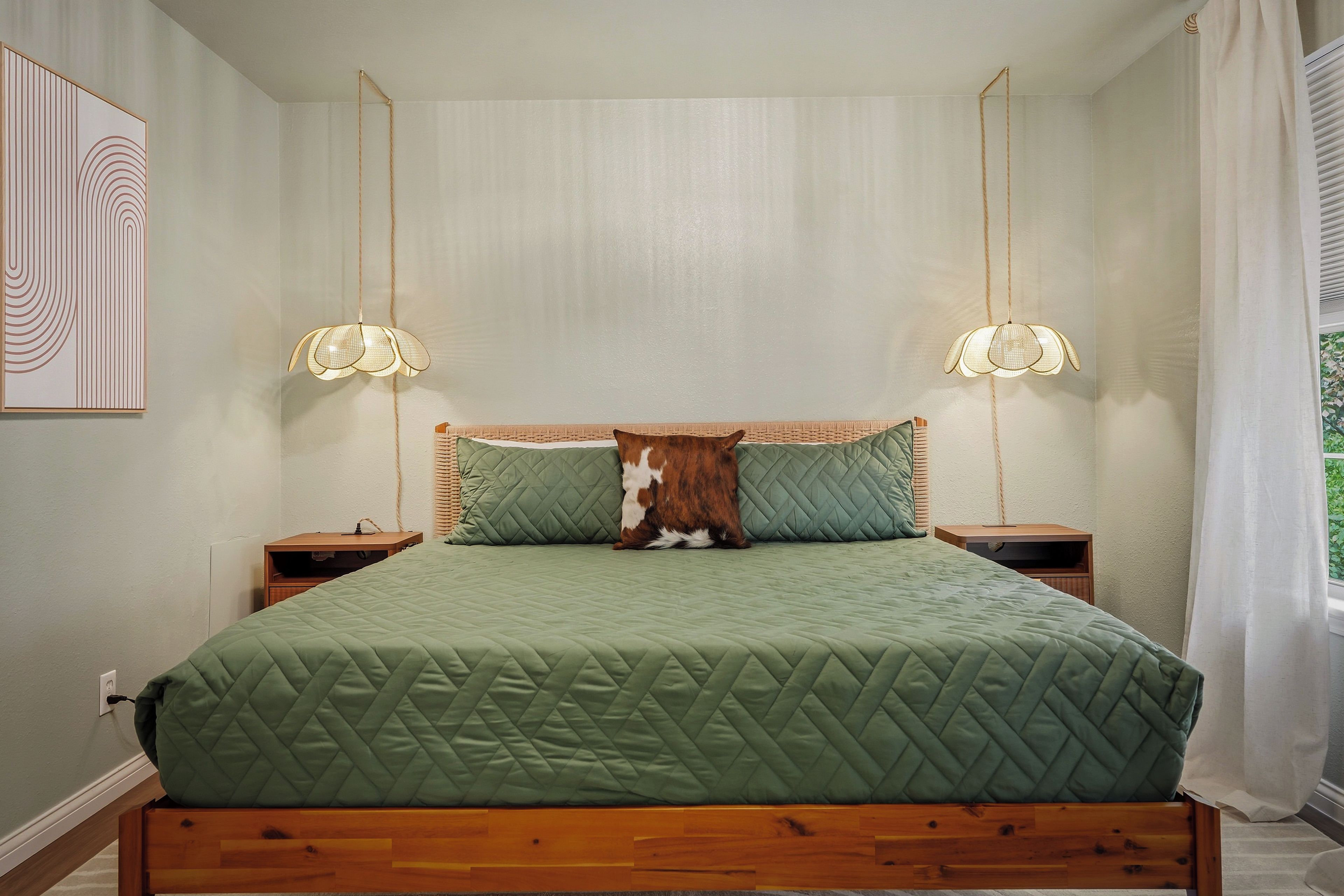A bed with a green quilted bedspread, two nightstands with lamps, a pillow with a brown and white pattern, and a wall with a framed abstract design.