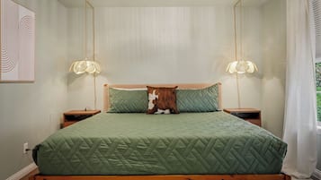 A bed with a green quilted bedspread, two nightstands with lamps, a pillow with a brown and white pattern, and a wall with a framed abstract design.