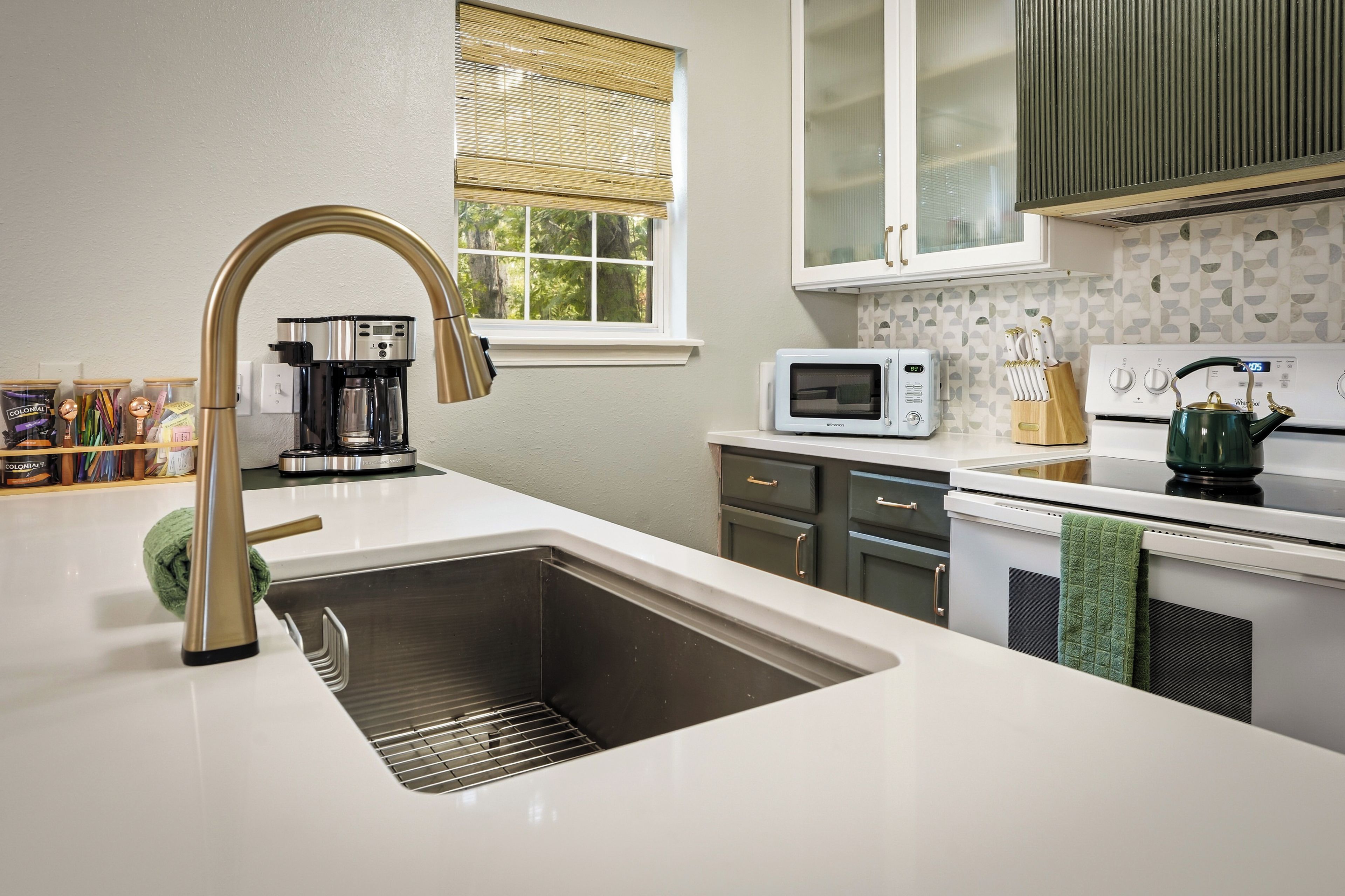 A modern kitchen with a stainless steel sink, a coffee maker, a microwave, and a kettle.