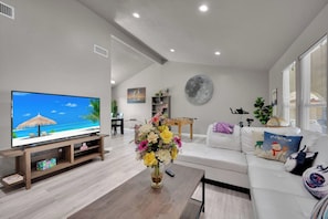 Ein modernes Wohnzimmer mit einem Flachbildfernseher, einem weißen Sofa, einem Couchtisch und einer dekorativen Vase mit Blumen.