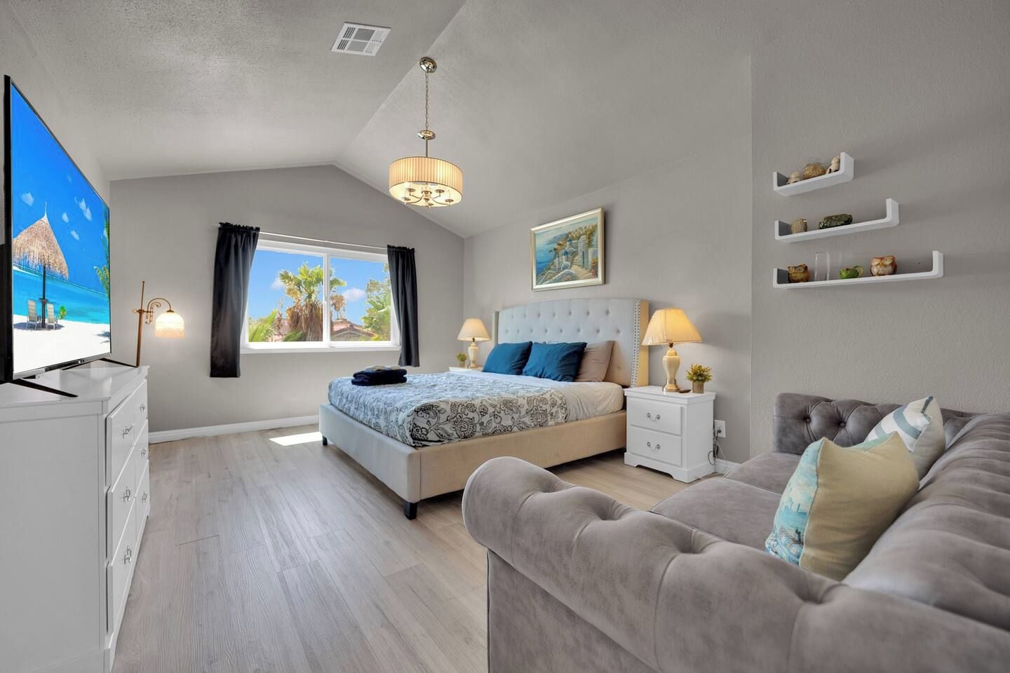 A modern bedroom with a bed, bedside tables, a TV, a sofa, and a window with curtains.