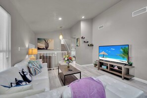 Ein modernes Wohnzimmer mit Flachbildfernseher, einer Couch, einem Couchtisch und einer Treppe, die in ein Obergeschoss führt.