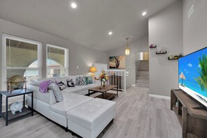 A modern living room with a white sofa, a coffee table, and a flat-screen TV. - Travelers Dream|Monthly Stays|Strip in the Horizon (Las Vegas)
