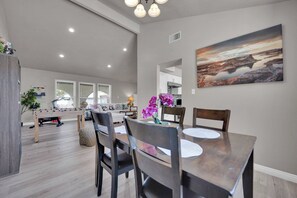 A dining area with a table and chairs, a painting on the wall, and a view into the kitchen. - Travelers Dream|Monthly Stays|Strip in the Horizon (Las Vegas)