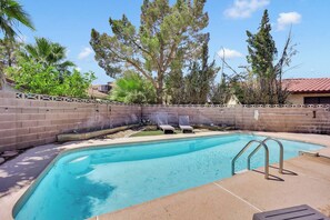 A swimming pool with a brick wall, lounge chairs, and trees. - Travelers Dream|Monthly Stays|Strip in the Horizon (Las Vegas)
