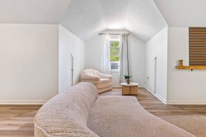 Een moderne, minimalistisch ingerichte kamer met een gebogen bank, een enkele stoel, een klein rond tafeltje en een raam met gordijnen.