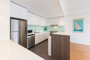 Eine moderne Küche mit Edelstahlgeräten, weißen Schränken und einer Wand in Holzoptik.