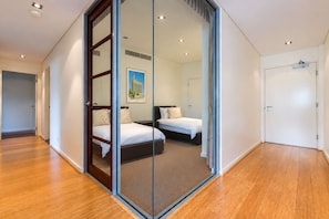 A modern hotel room with a glass partition, wooden flooring, and a bed with white bedding. - Central Freo 3BR Apartment, Pool, Gym & parking (Fremantle)