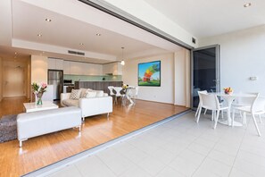 Ein modernes Wohnzimmer mit einer Couch, einem Esstisch und Stühlen. Es gibt eine Küchenzeile mit Schränken und einem Kühlschrank.