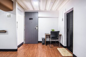 A room with a wooden floor, a desk with a chair, a door labeled '201', and a small plant on the desk.
